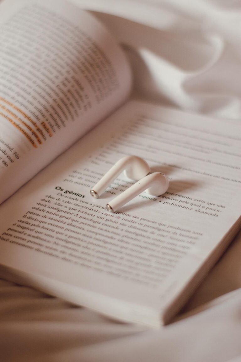 AirPods resting on an open book with soft fabric background, creating a cozy atmosphere.